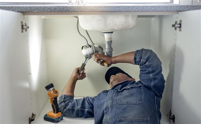 Plumber repairing pipes beneath a bathroom sink in Hialeah