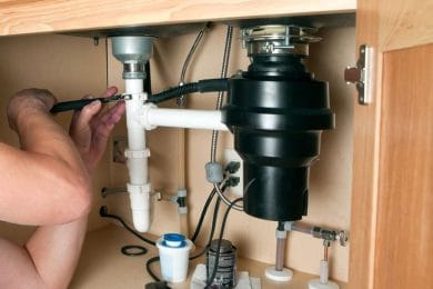 Plumber repairing a garbage disposal beneath a kitchen sink in Hialeah