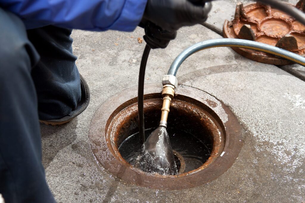 Plumber hydro jetting a sewer line through a manhole in Hialeah