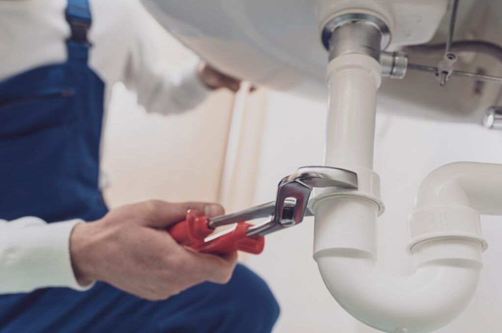 Plumber repairing a white drain pipe beneath a sink in Hialeah
