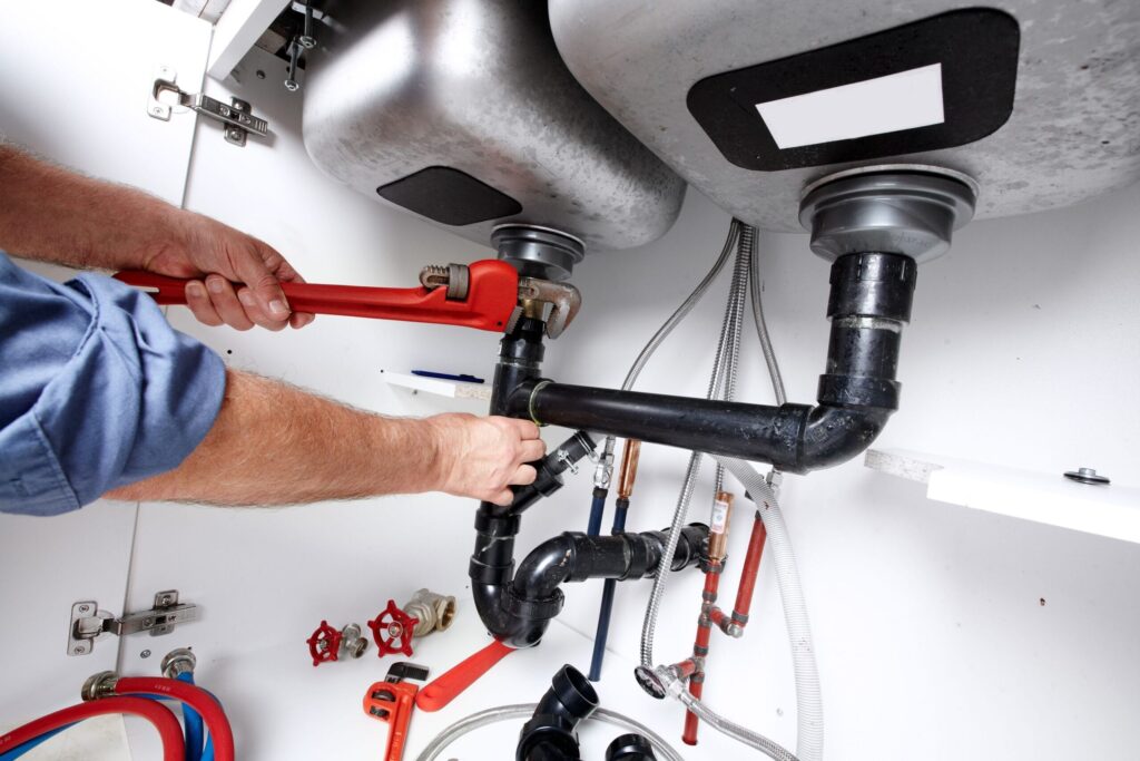 Plumber repairing drain pipes beneath a kitchen sink in Hialeah